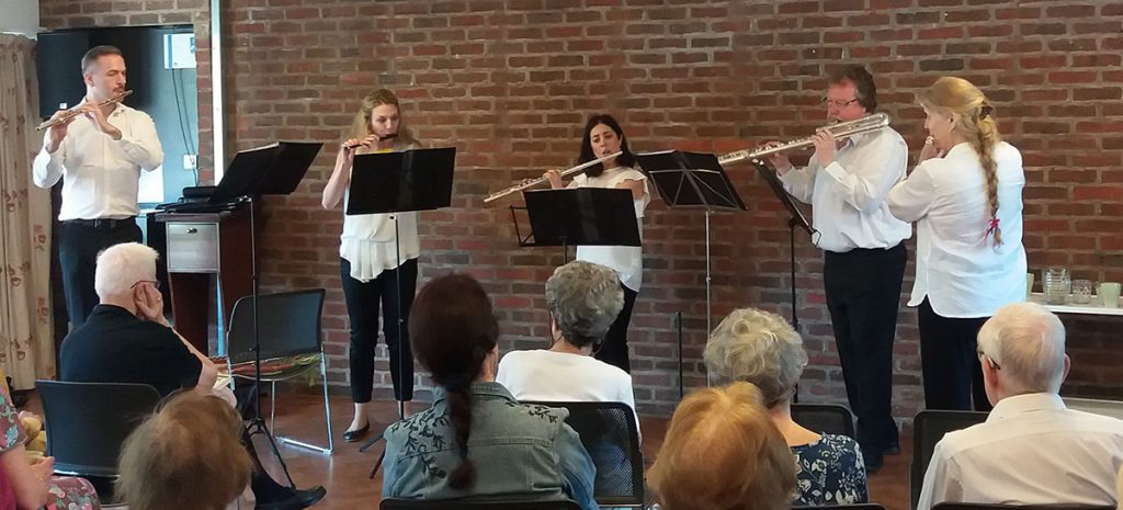 Three men and two women playing the flute in front of an audience