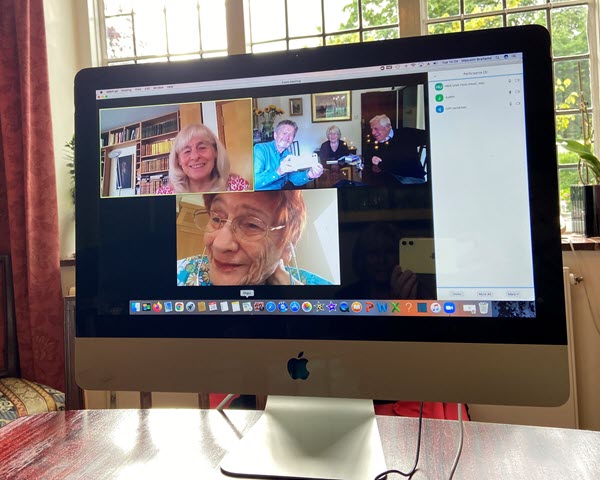 Computer screen showing members meeting online and in a private home