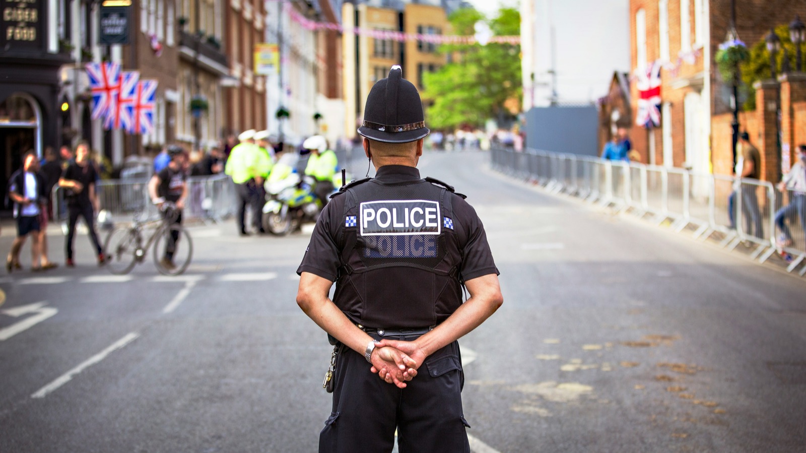 Police constable with his arms behind his back looking down a street bedecked with union flags.