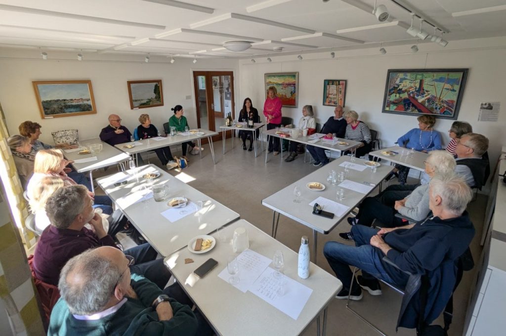 Group of people sitting at tables listening to a description of a wine